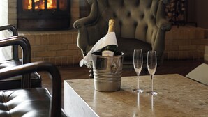 A cozy room with a fireplace, a plush armchair, a table with a bottle of champagne and glasses, and a ship model on the wall. - Hótel Búðir (Snæfellsbær)