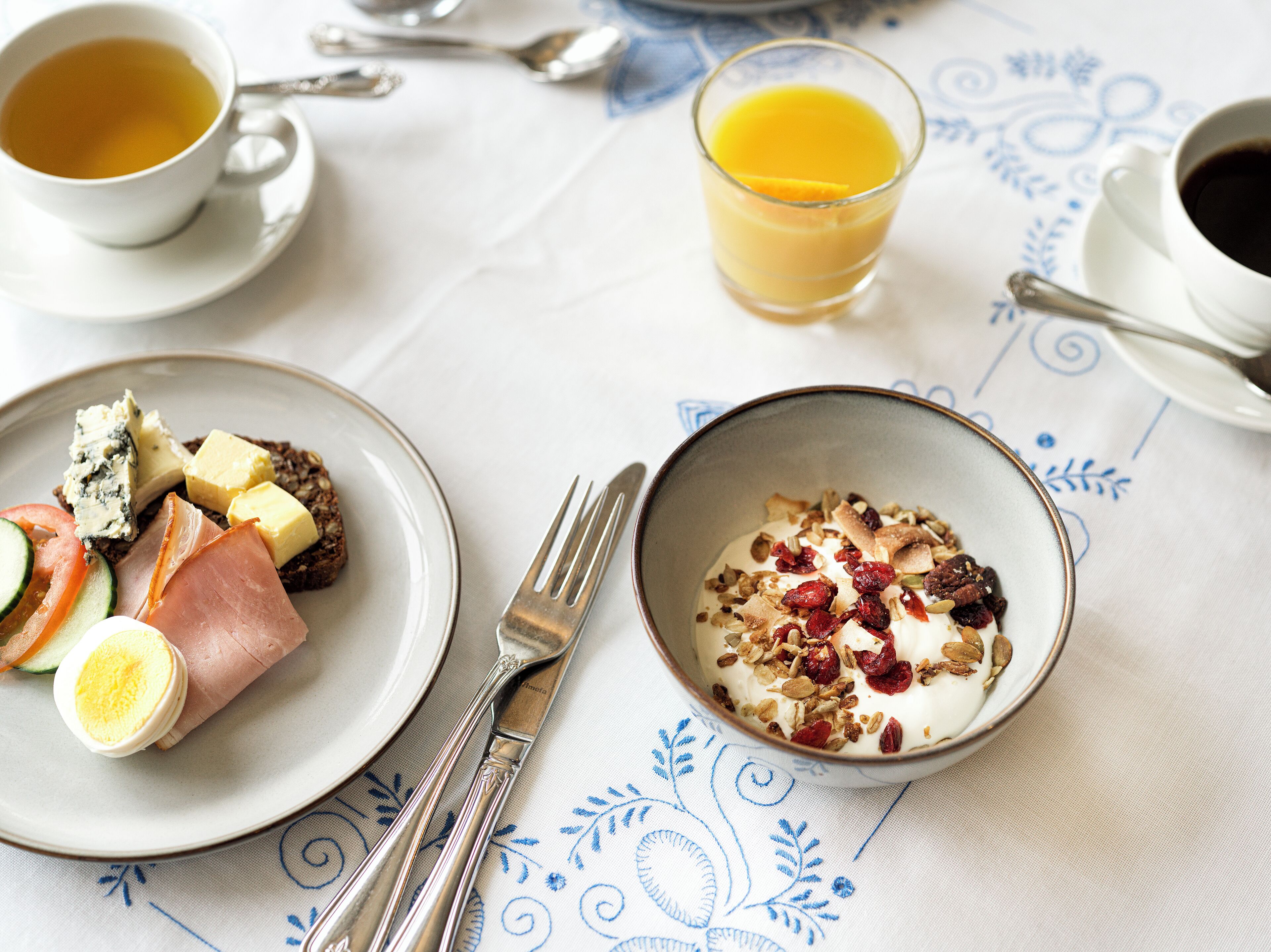 Una mesa de desayuno con platos de comida, un vaso de jugo de naranja y una taza de café.