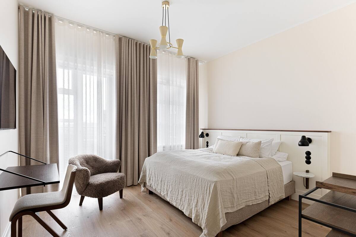 Una habitación de hotel con una cama, una silla, un escritorio y una lámpara.