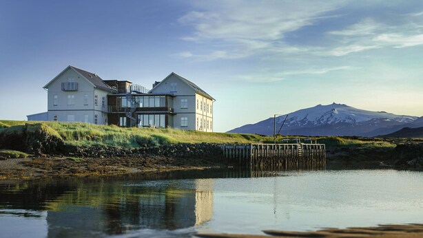 A two-story house with a large balcony, a staircase, and a view of a mountain in the background. - Hótel Búðir (Snæfellsbær)