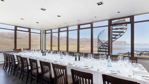 A long dining table set for a meal with chairs, large windows, and a view of mountains and water. - Hótel Búðir (Snæfellsbær)