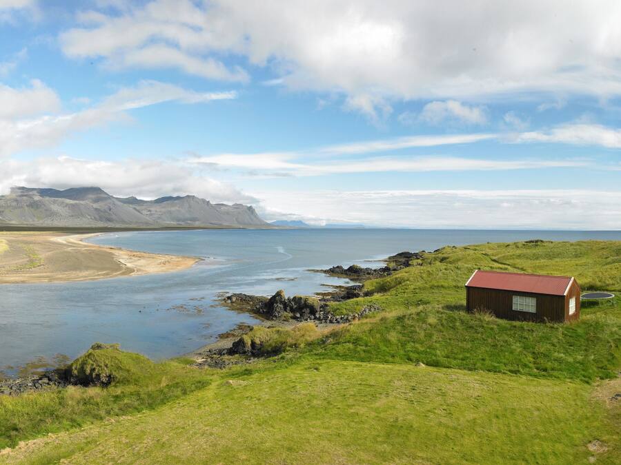 A coastal landscape with a small cabin, a dock, and a grassy area.