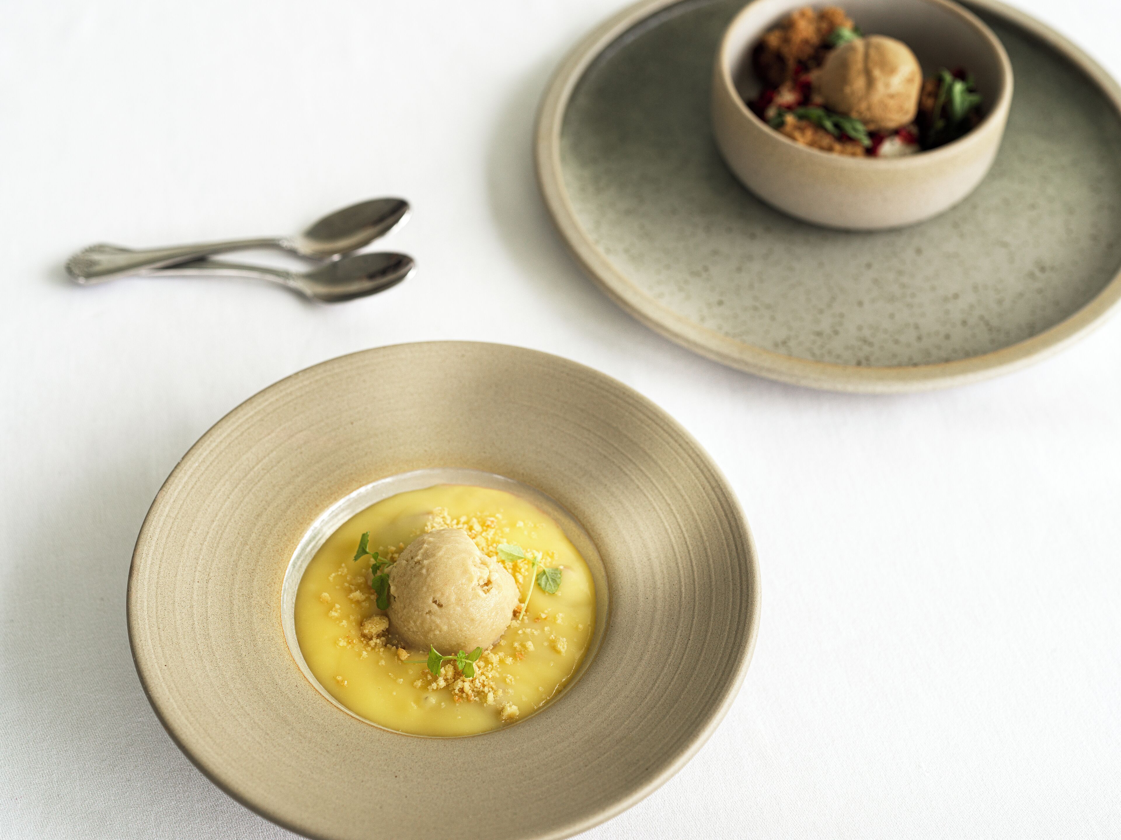 Un plato de postre con un dulce esférico y un tazón de sopa sobre una mesa.