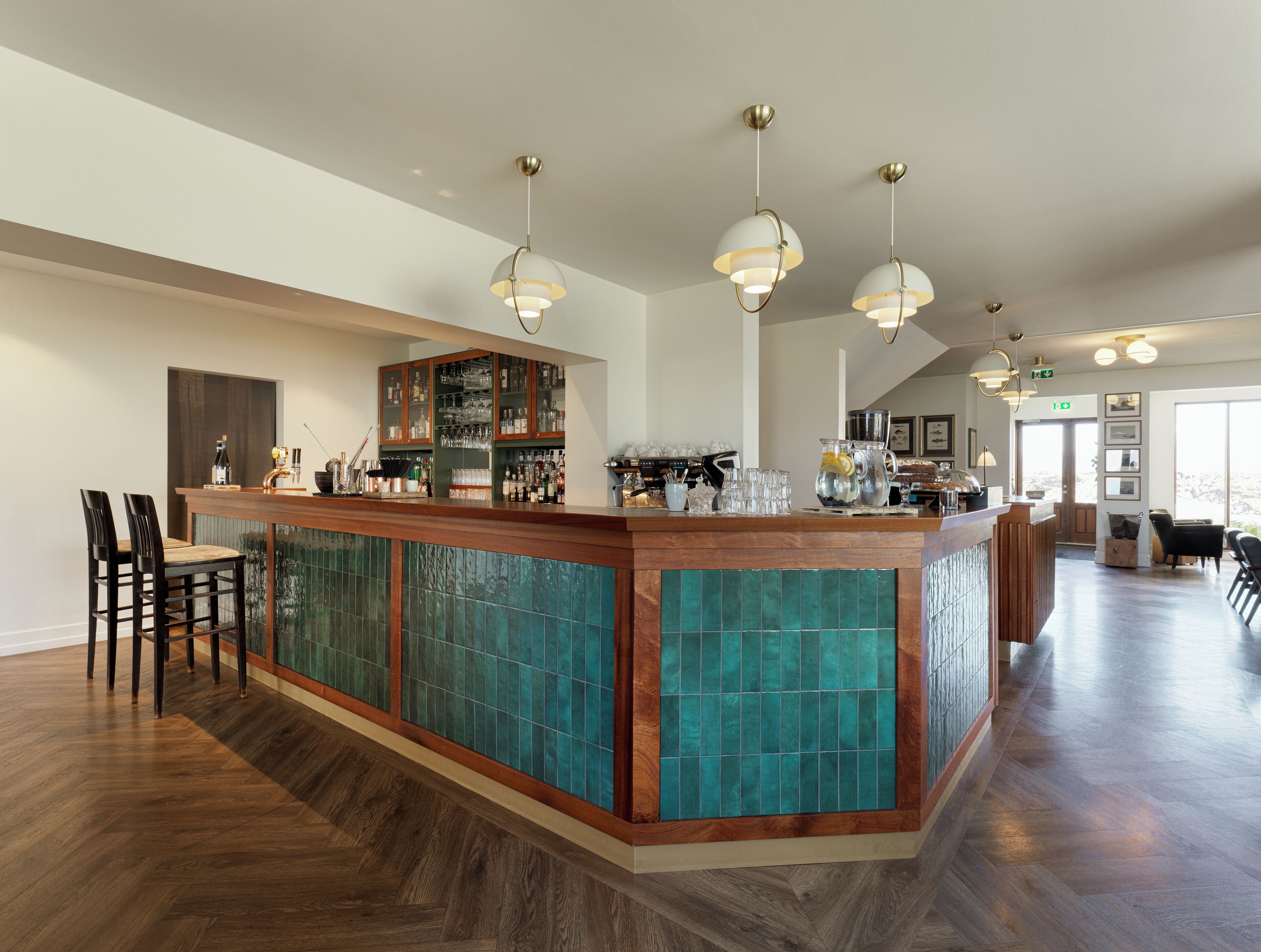 Un espace bar doté d’un comptoir en bois, de luminaires suspendus et d’un mur recouvert de carreaux.