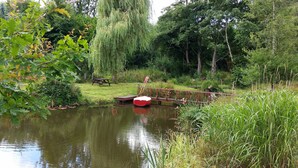 A serene pond with a wooden dock and picnic table, surrounded by lush greenery and trees. - Charming English cottage, Ashdown Forest, excellent pub (Danehill)