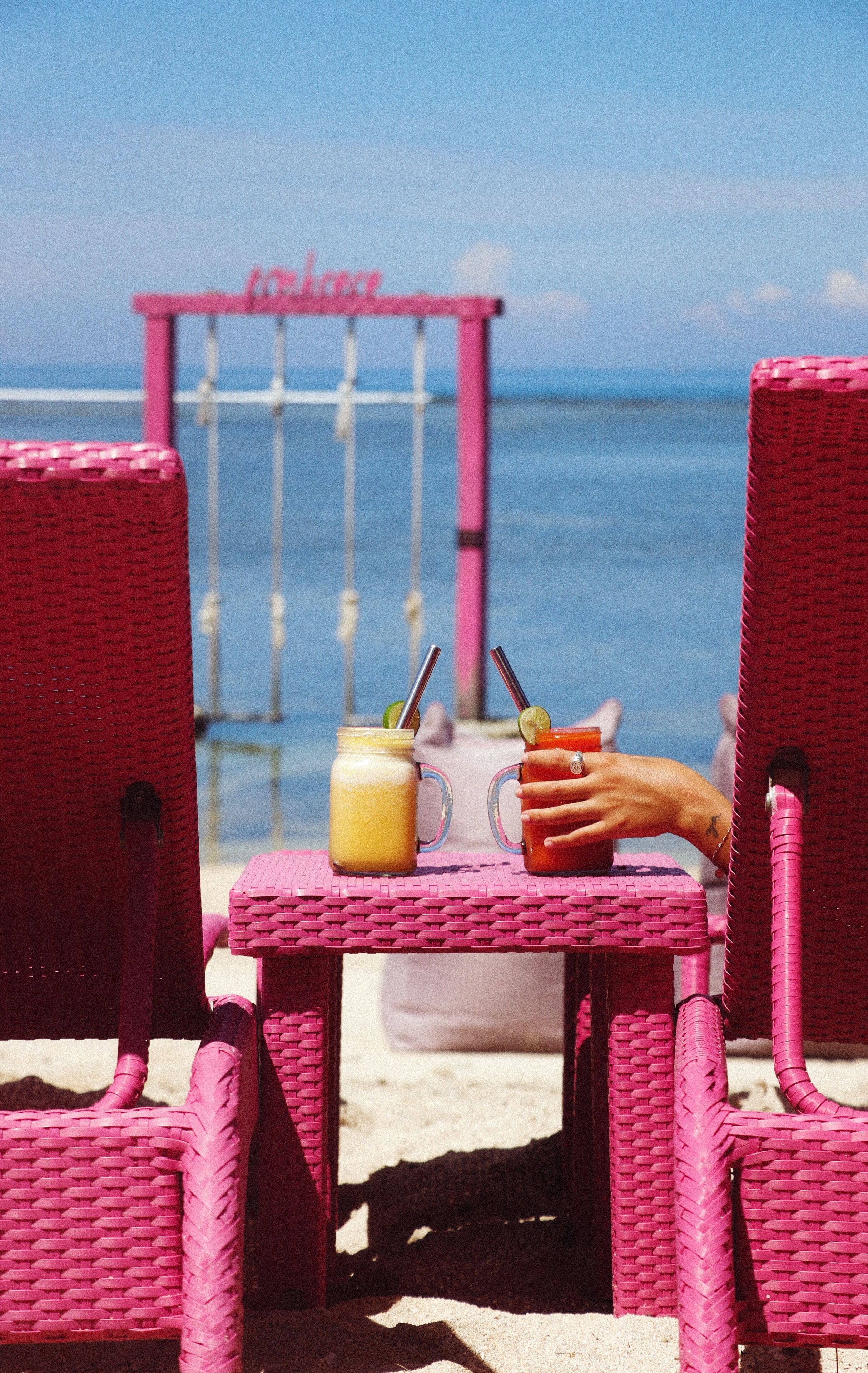 A beach scene with two wicker chairs and a table.