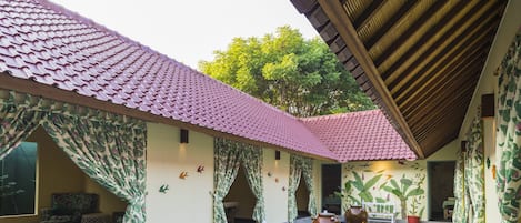 Un patio con techo de tejas, una fuente con jarrones y una zona de estar con cortinas estampadas.