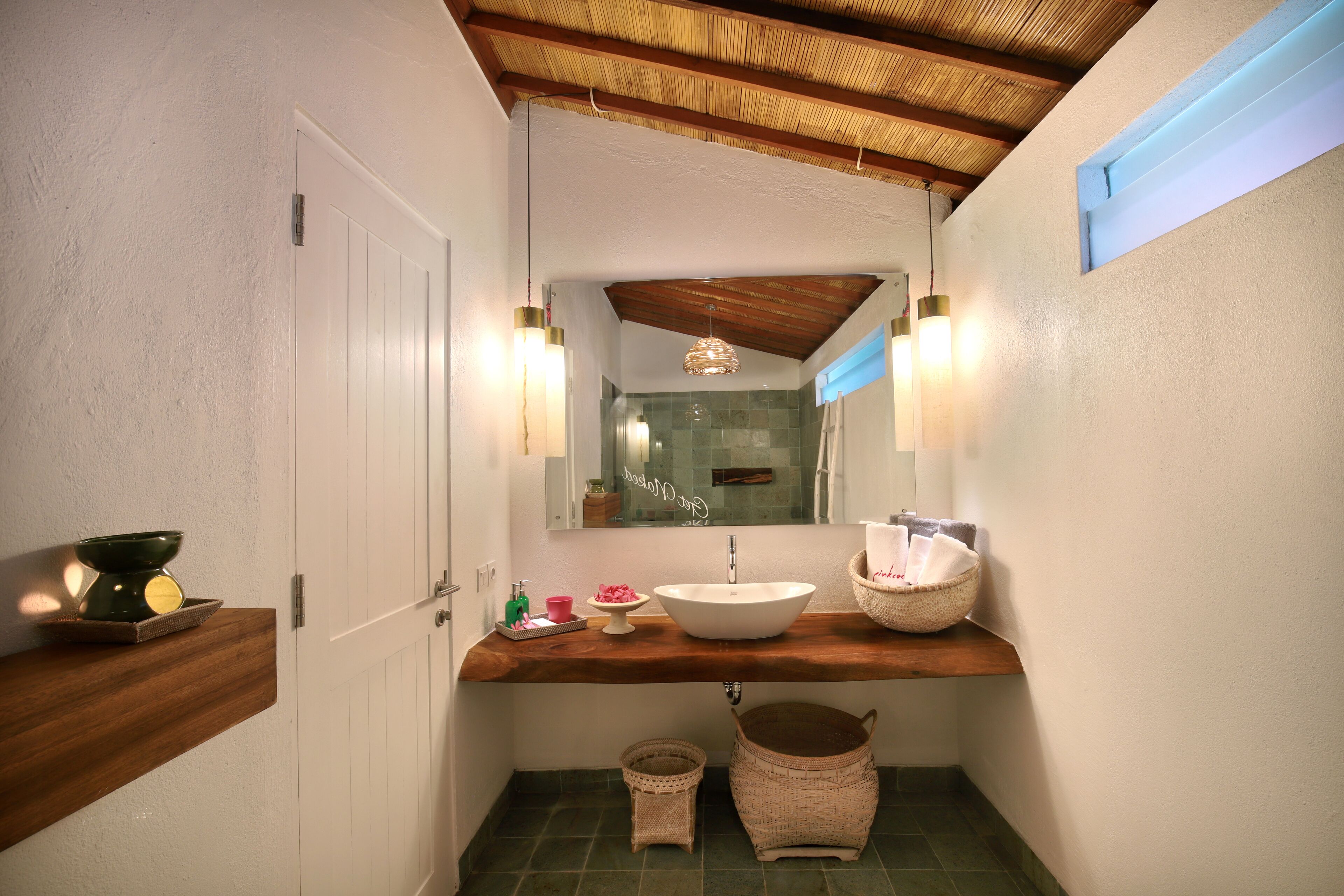 A bathroom with a wooden vanity, a large mirror, a white sink, and a shower area.