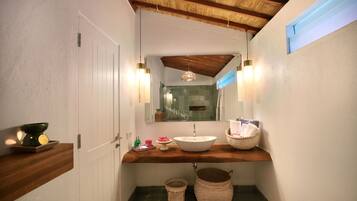 A bathroom with a wooden vanity, a large mirror, a white sink, and a shower area.
