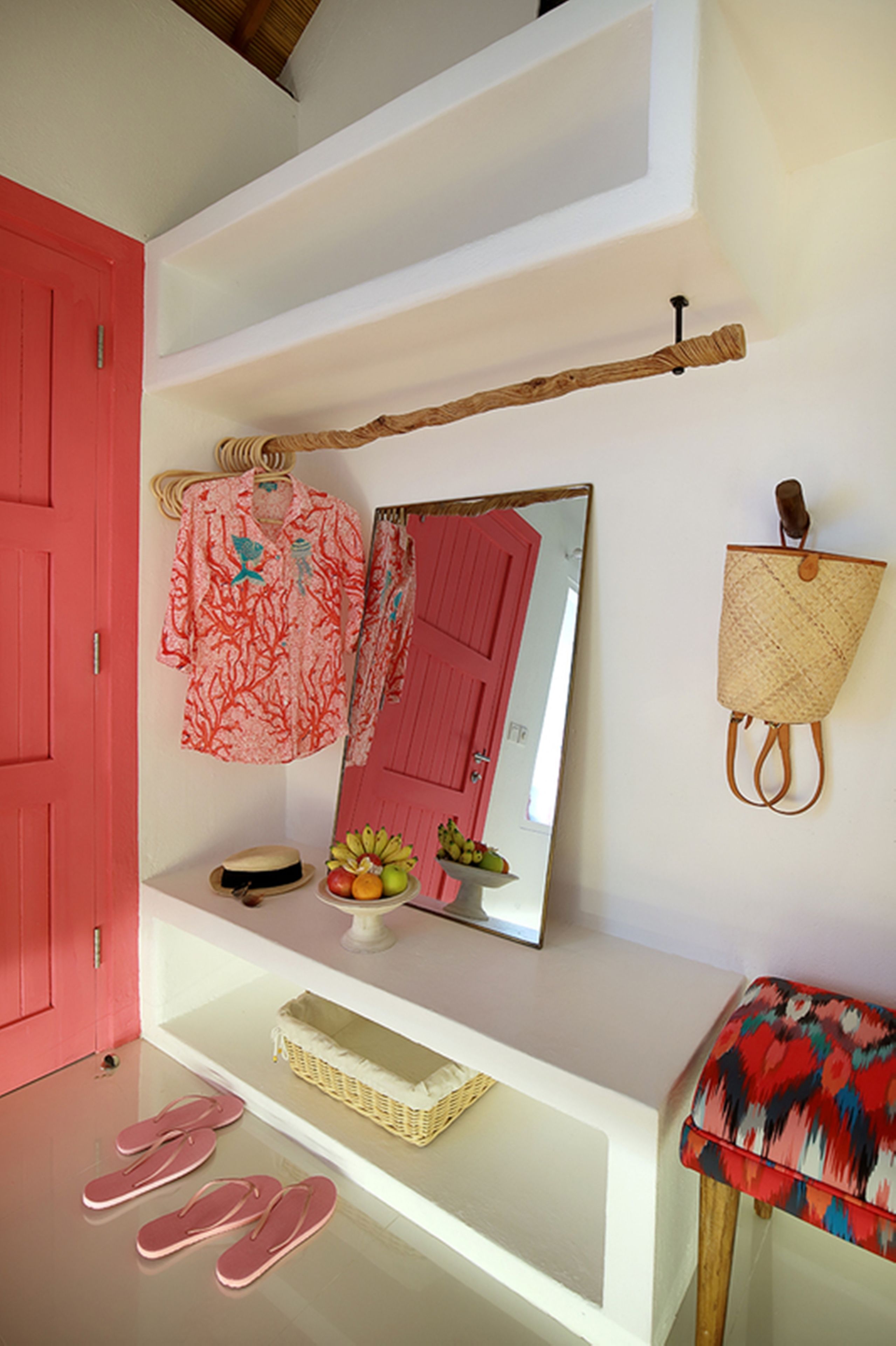 Una habitación con una puerta roja, un espejo, un estante con un sombrero, una cesta y un par de chanclas en el suelo.