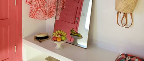 Una habitación con una puerta roja, un espejo, un estante con un sombrero, una cesta y un par de chanclas en el suelo.