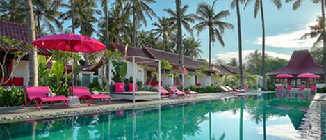A pool area with lounge chairs and umbrellas, surrounded by palm trees.