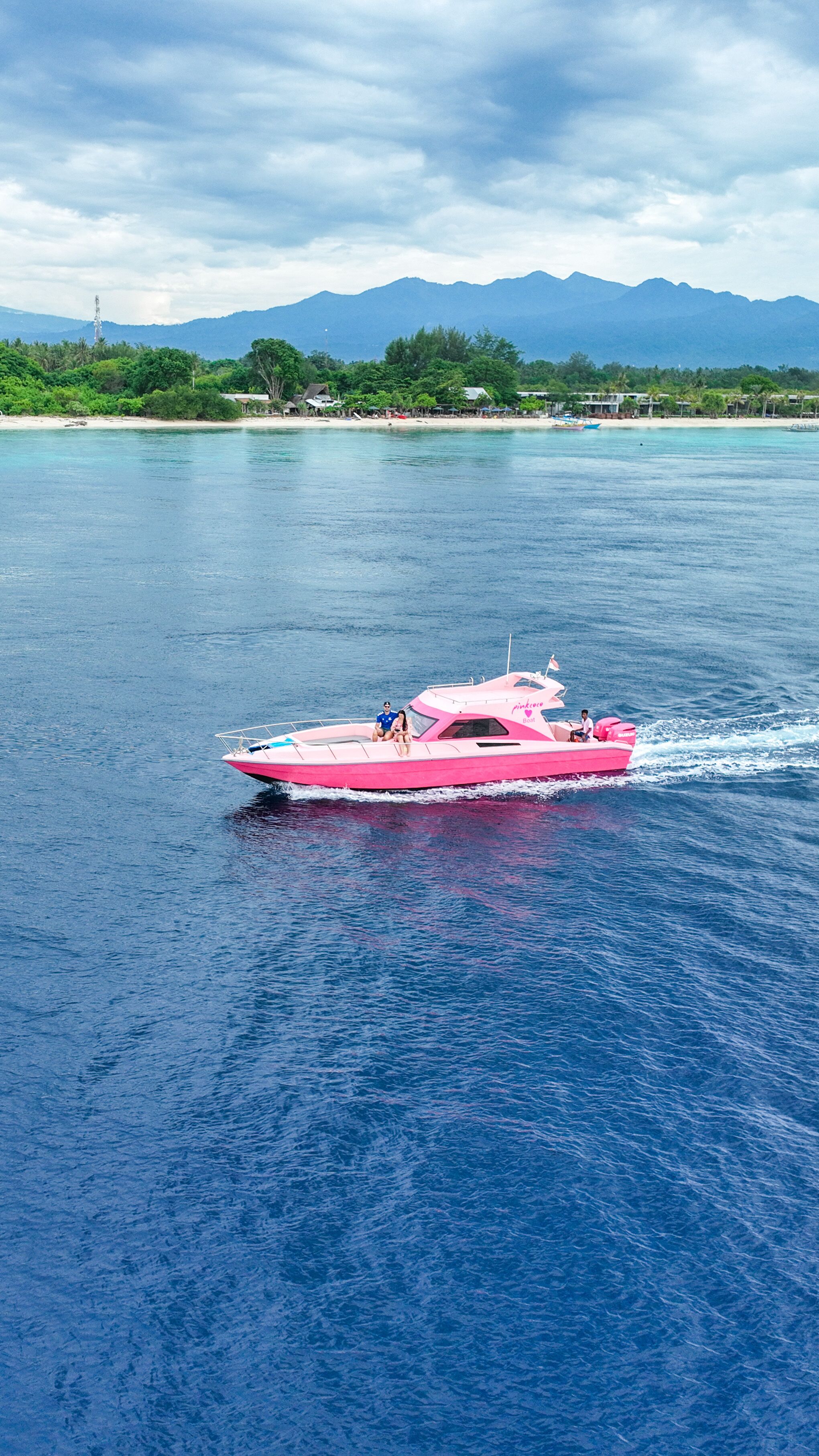 A pink speedboat on a calm sea with a mountainous backdrop.