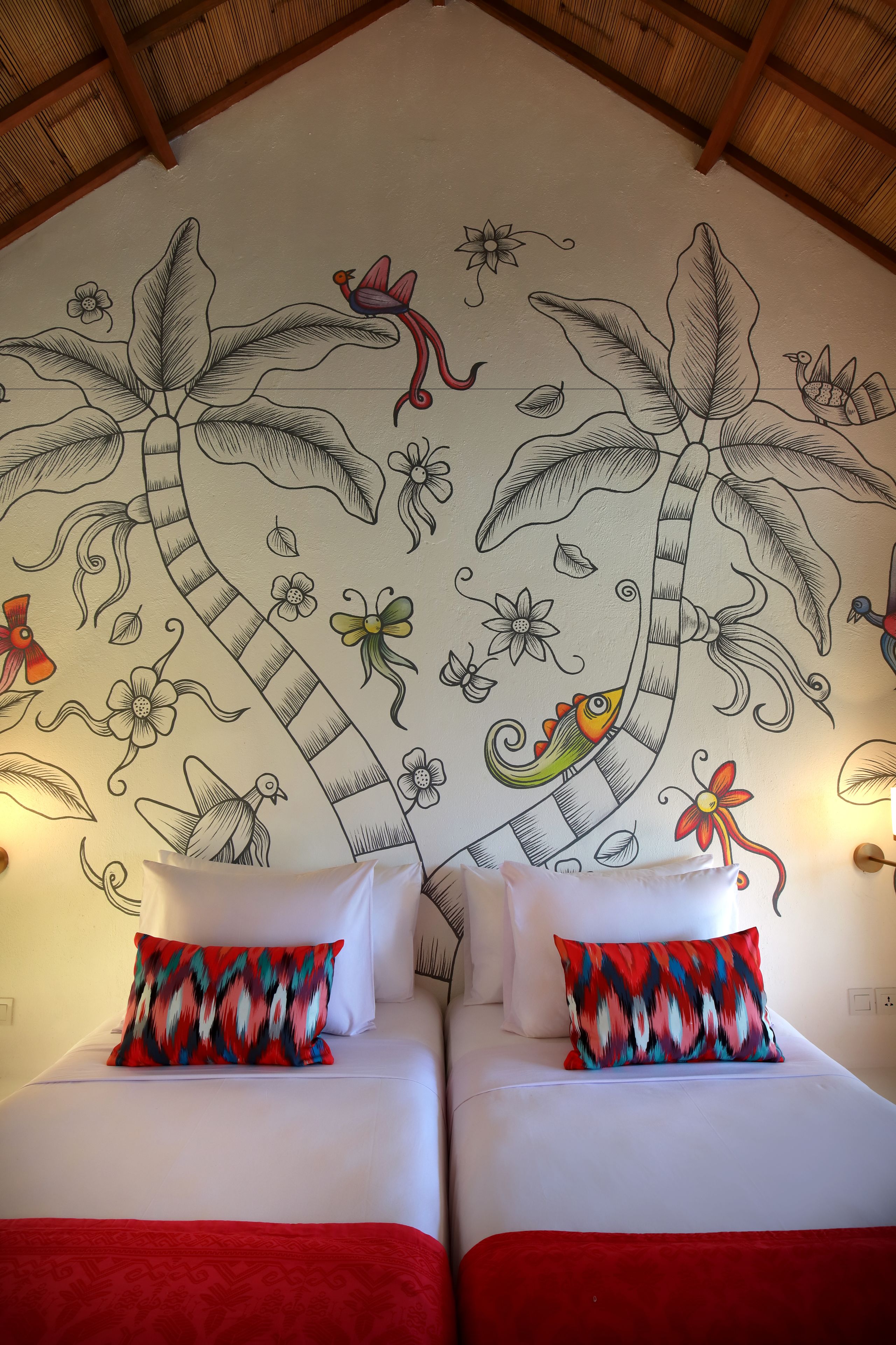 A room with two beds, each with a patterned pillow, and a large mural on the wall depicting tropical plants and birds.
