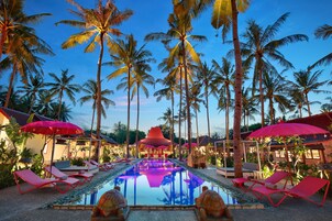 A pool area with lounge chairs and umbrellas, surrounded by palm trees.
