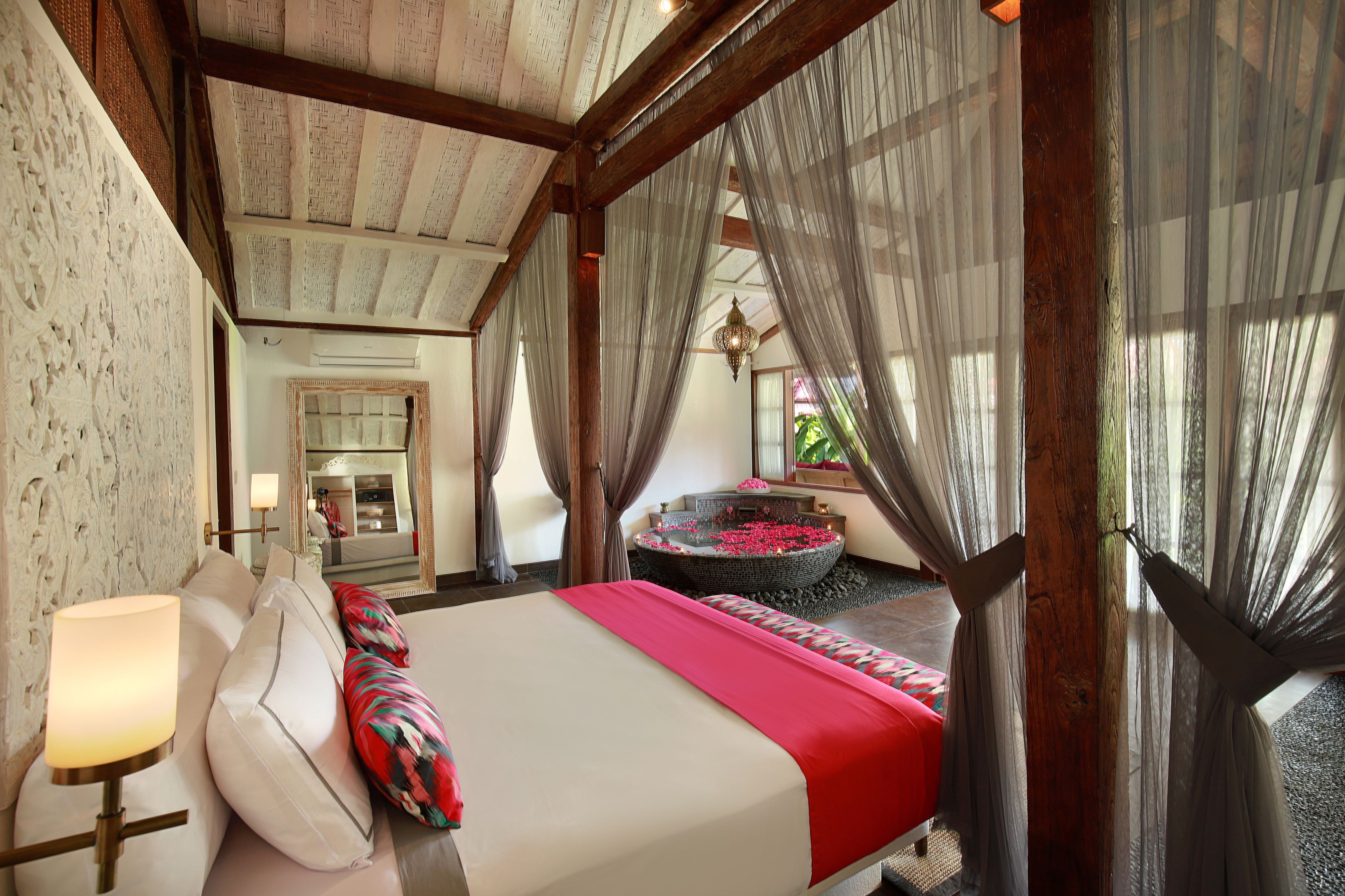 A bedroom with a large bed, a bedside table, and a view of a bathroom with a bathtub.