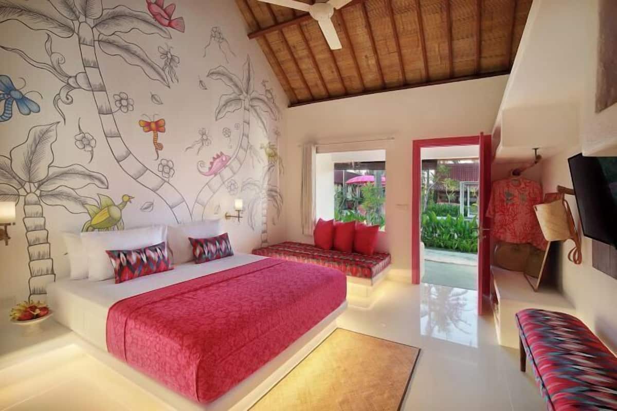 A bedroom with a large bed, a wall mural, a ceiling fan, and a view of the outdoors.