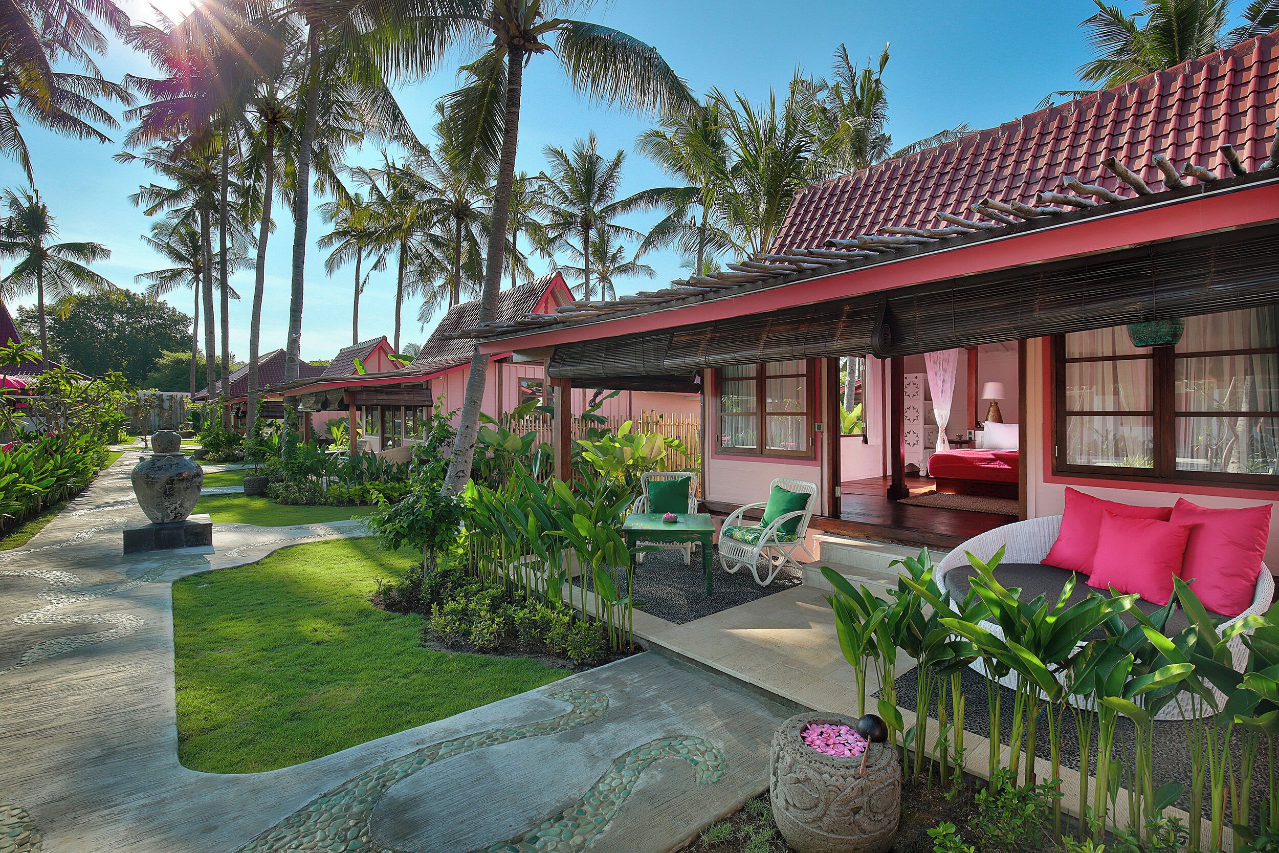 Un resort con techo de tejas rojas, un jardín con palmeras y un área de descanso con sofá y sillones.