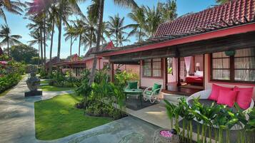 Un resort con techo de tejas rojas, un jardín con palmeras y un área de descanso con sofá y sillones.