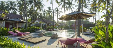 A resort pool area with lounge chairs, umbrellas, and palm trees.