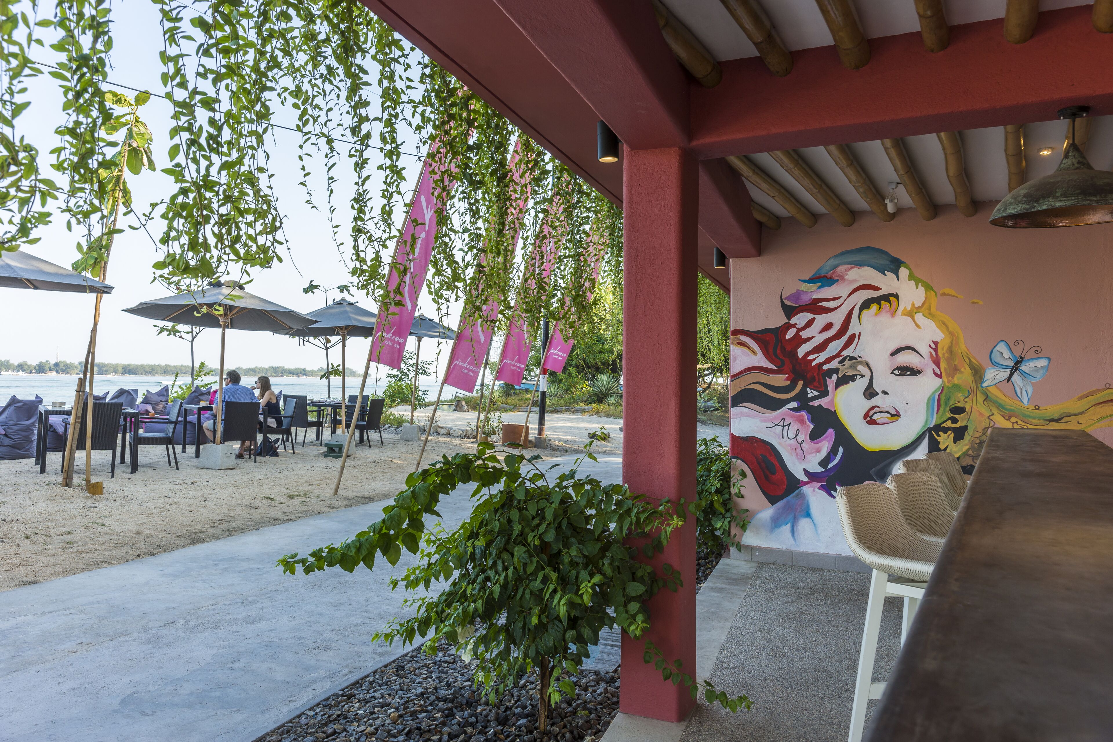 Un espace extérieur aménagé avec des tables et des chaises, une fresque murale et des plantes suspendues.