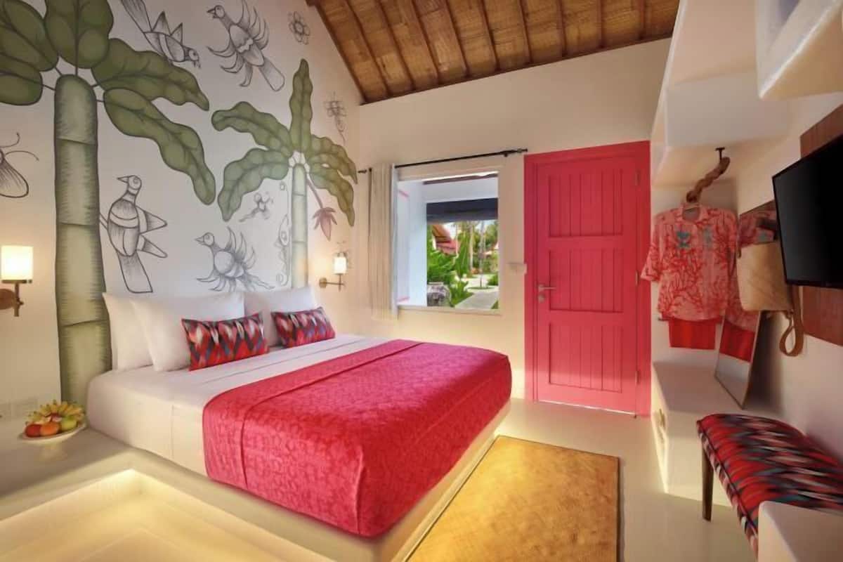 A bedroom with a bed, a red door, a window, and a wall mural.