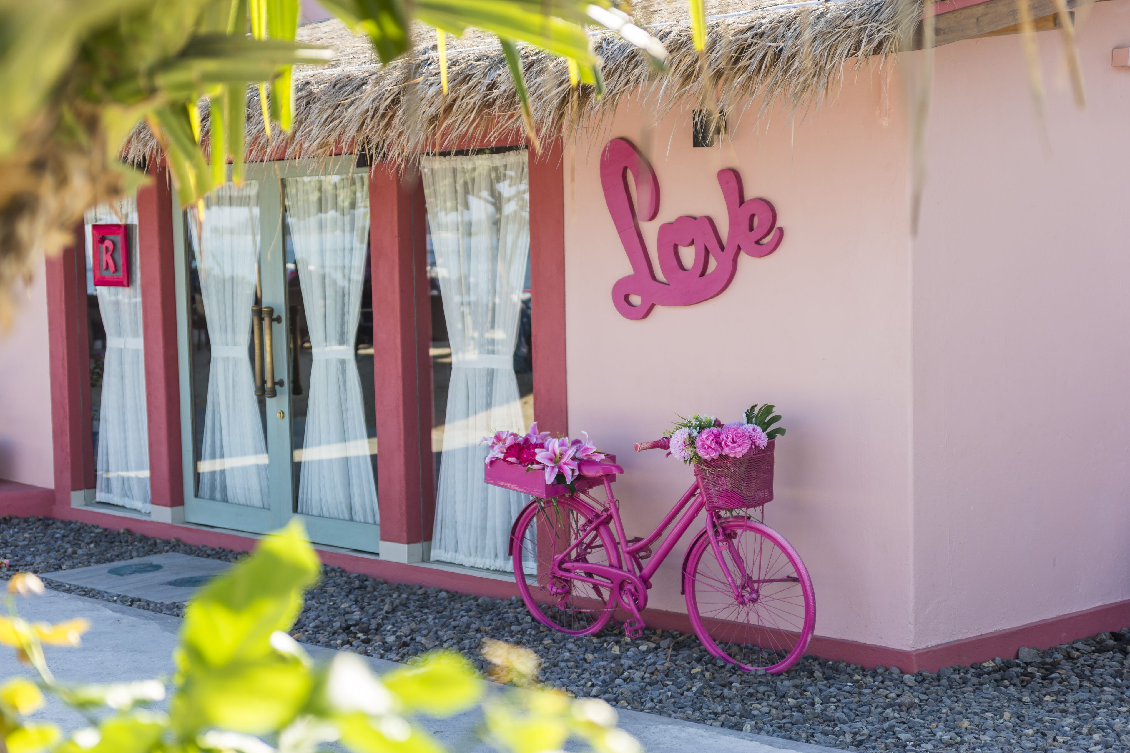 A pink building with a sign that reads "Lok" and a pink bicycle with baskets of flowers.