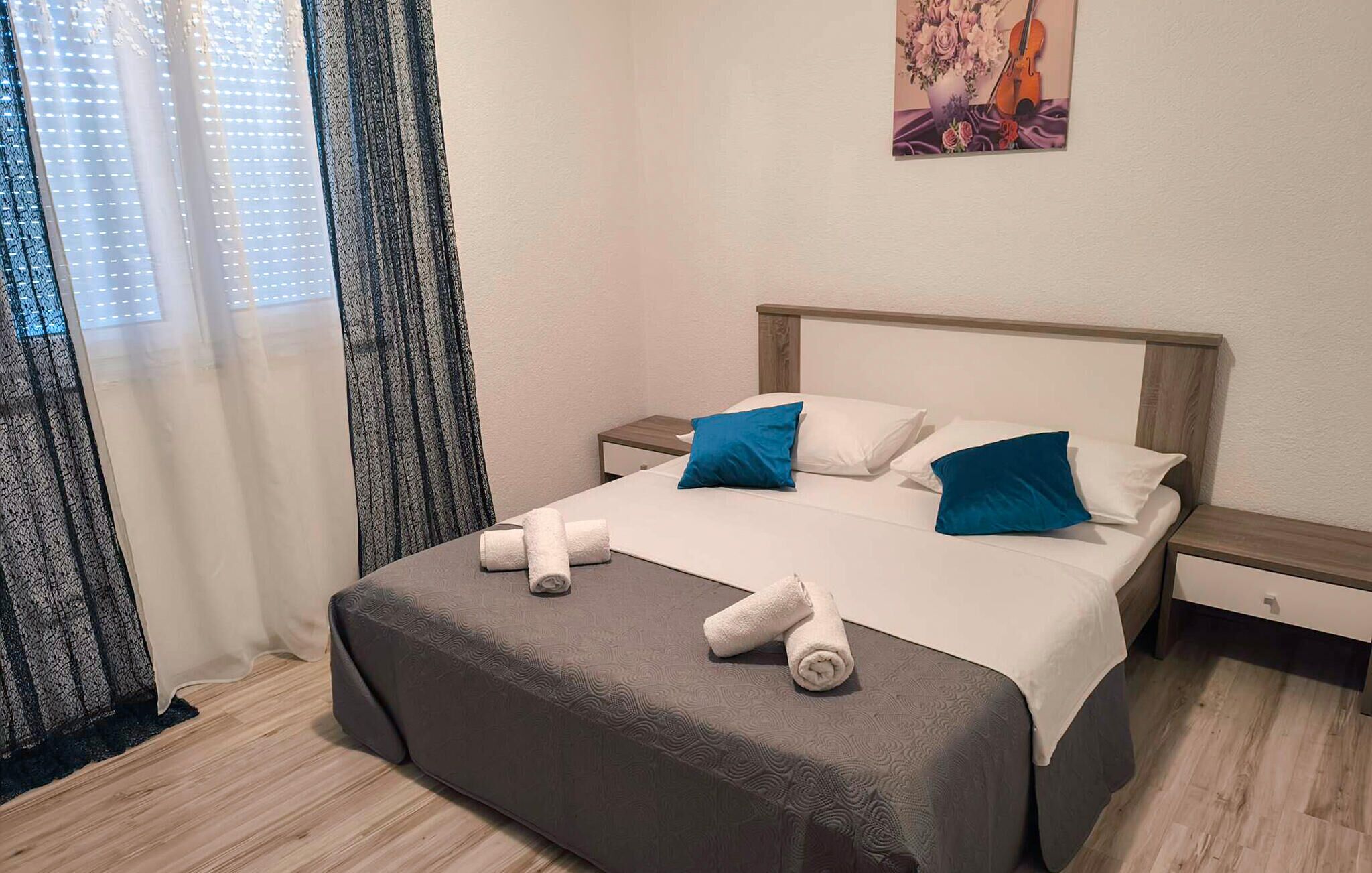 Uma cama bem arrumada com almofadas brancas e azuis, uma cabeceira de madeira e uma pequena mesa de cabeceira com um abajur.