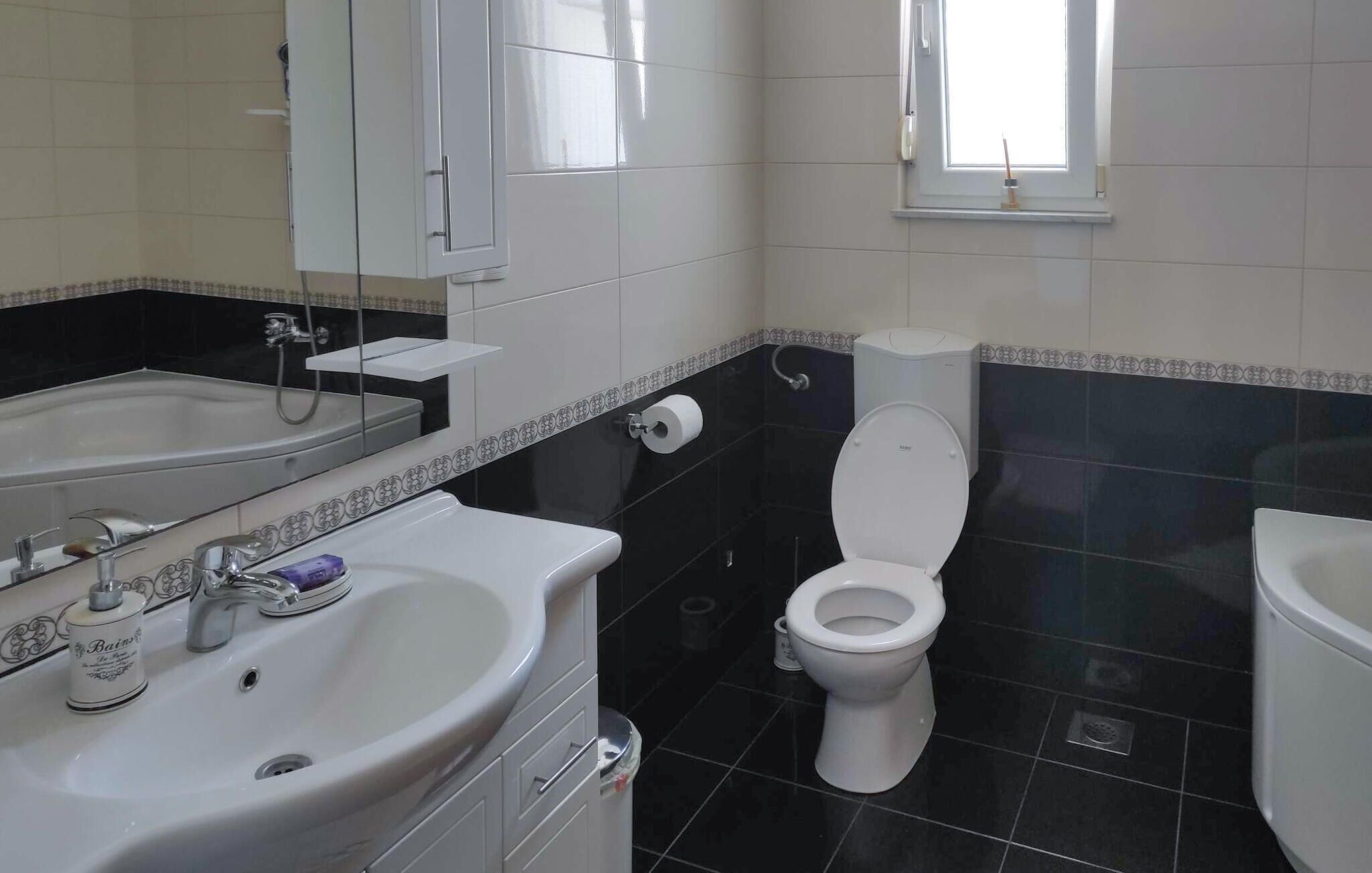 A bathroom with a white sink, mirror, and toilet. There is a window above the toilet.