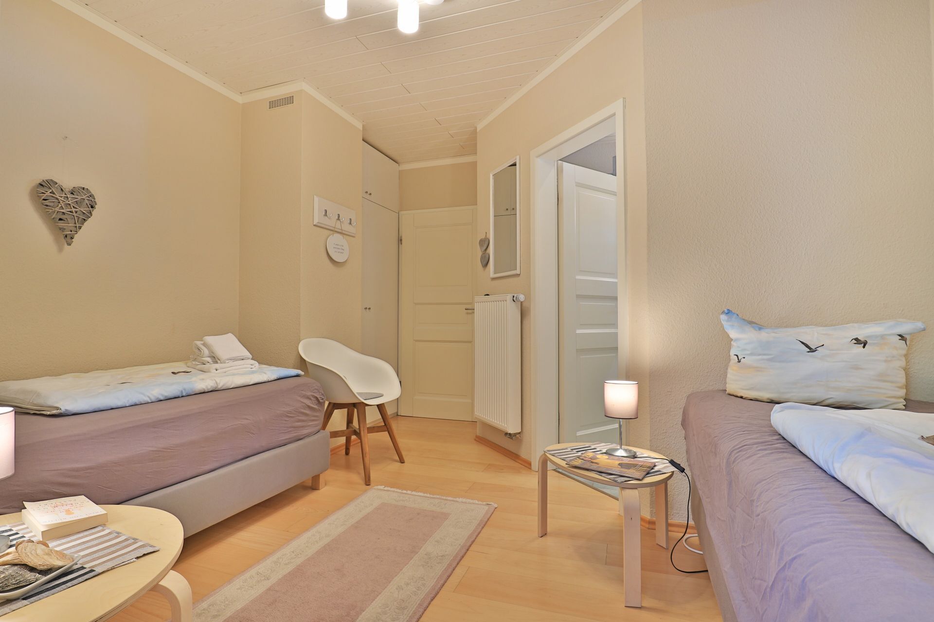 A compact bedroom with two single beds, a small table with a lamp, and a chair.