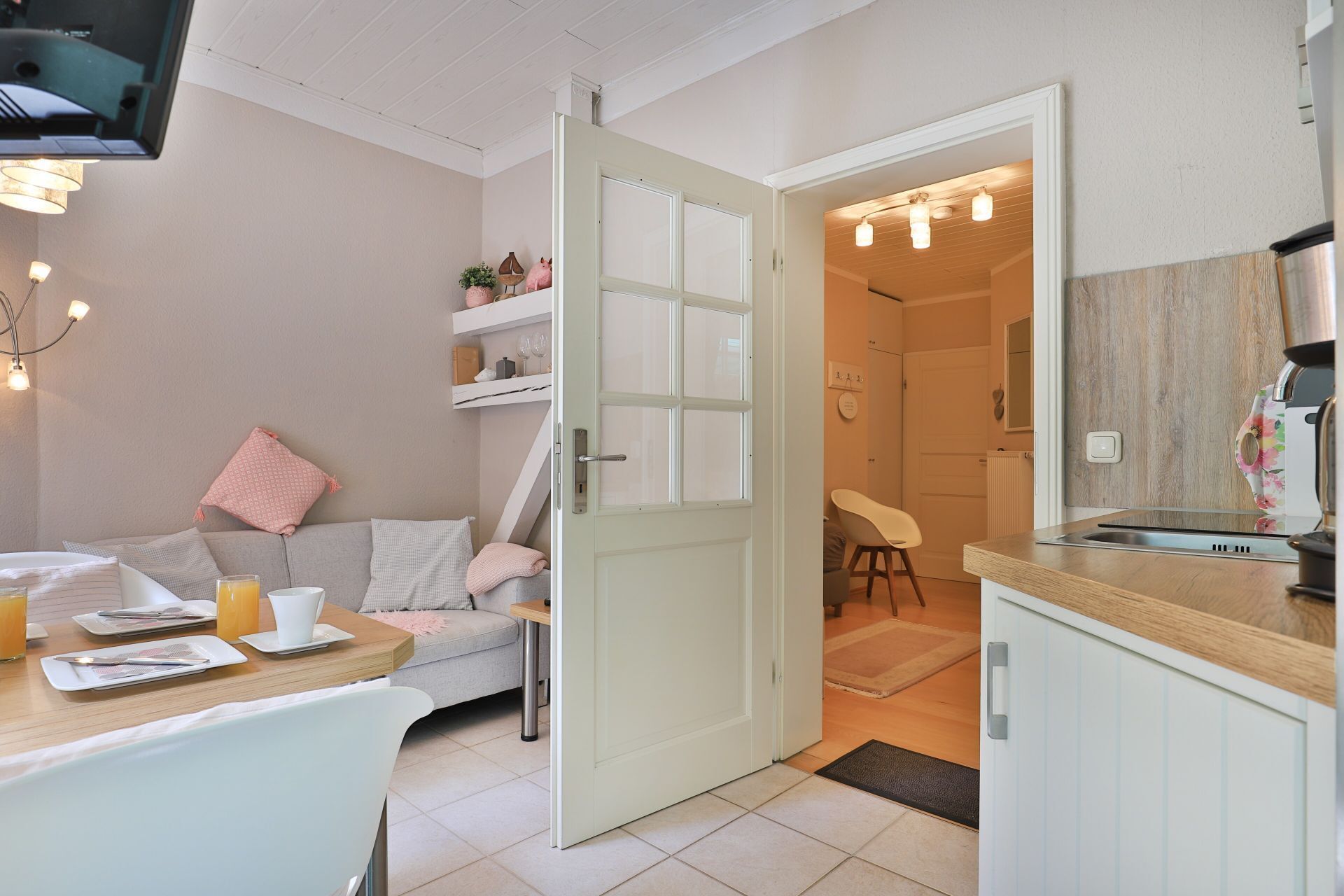 Ein gemütliches Zimmer mit Essbereich, einer Couch, einer Küche mit Kaffeemaschine und einer Tür zu einem weiteren Raum.