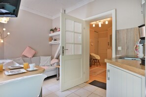 Een gezellige kamer met een eethoek, een bank, een keuken met een koffieapparaat en een deur naar een andere kamer.