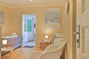 Une chambre à coucher avec un lit, une table de chevet avec une lampe, une chaise, un tableau et une porte.