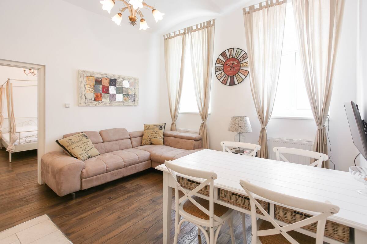Een woonkamer met een beige modulaire bank, een witte eettafel en een grote wandklok.