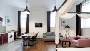 A modern, well-lit room with a wooden dining table, a sofa, a bed, and a washing machine.