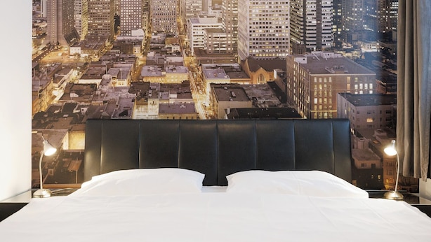 A hotel room with a large bed, a city view, and two bedside lamps.