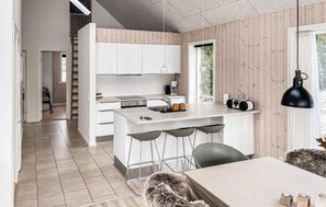 A modern kitchen with white cabinets, a central island, bar stools, and a dining table.