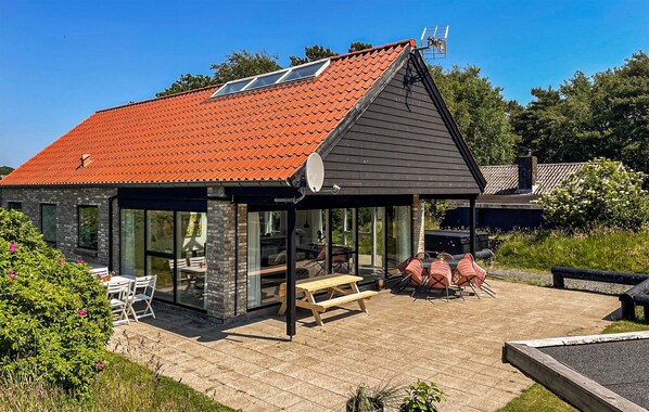 Una casa moderna con techo de tejas rojas, un porche cubierto con mobiliario exterior y una antena parabólica.