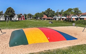 Una playa con una estructura de arena colorida, un área con césped y casas al fondo.