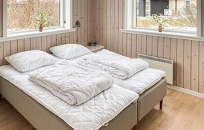 Una cama con ropa de cama blanca, una mesita de noche con una lámpara y una ventana con vistas a un paisaje nevado.
