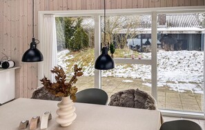 A room with a large window, a table with a vase, and two black pendant lights.