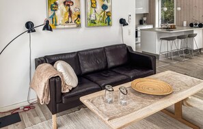 Uma sala de estar moderna com um sofá de couro preto, uma mesa de centro de madeira com velas e obras de arte na parede.