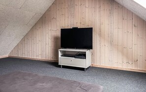 Una habitación con techo inclinado, pared de madera, un mueble blanco con televisor de pantalla plana y alfombra gris.