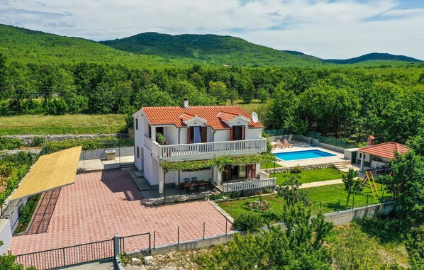 Una casa de dos pisos con techo de tejas rojas, un balcón y una piscina.