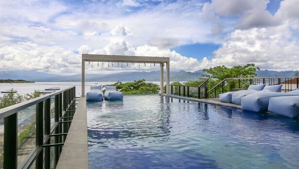 A pool area with a view of the sea and mountains, a pergola with hanging lights, and a seating area with cushions. - Marc Hotel Gili Trawangan (Gili Trawangan)