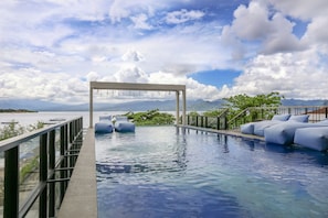 A pool area with a view of the sea and mountains, a pergola with hanging lights, and a seating area with cushions. - Marc Hotel Gili Trawangan (Gili Trawangan)