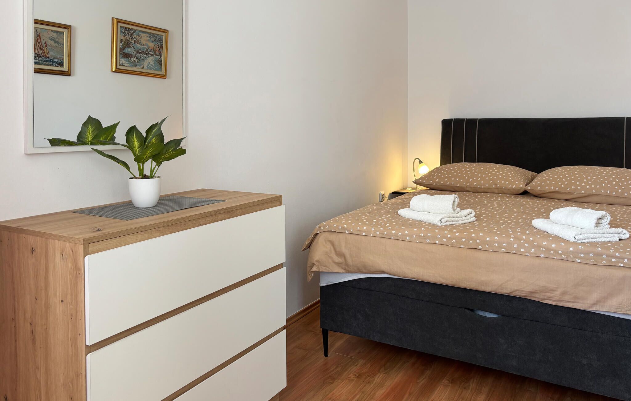Una camera da letto ordinata con un letto, un comodino e una pianta in vaso.
