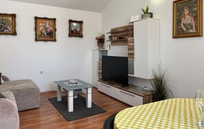 Un salon moderne doté d’un téléviseur à écran plat, d’une table basse en verre, d’un canapé et d’un coin repas avec une nappe à carreaux.
