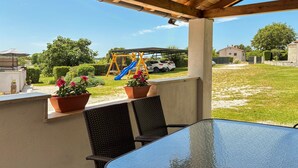 A covered patio with a table and chairs, a playground with a slide, and potted plants. - 1 bedroom nice home in Zminj (Zminj)