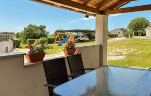 Eine überdachte Terrasse mit Tisch und Stühlen, ein Spielplatz mit Rutsche und Kübelpflanzen.